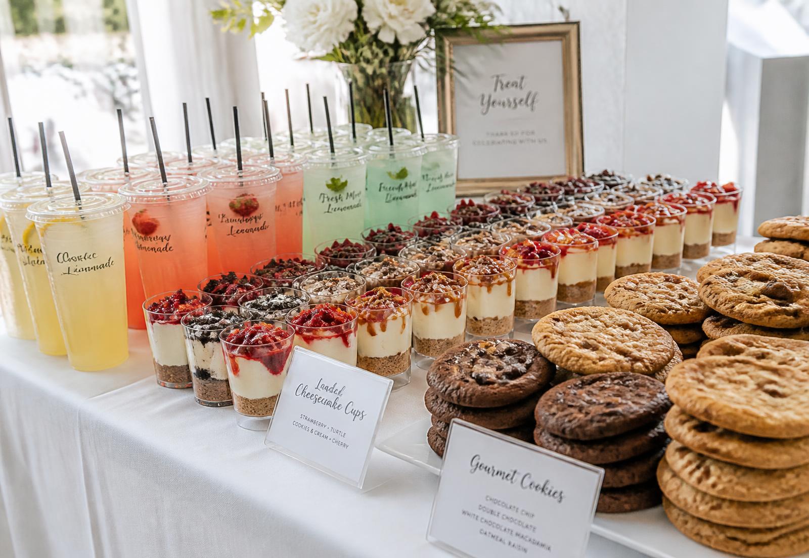 Catering dessert table with rows of lemonades, cheesecake cups, and stacked gourmet cookies